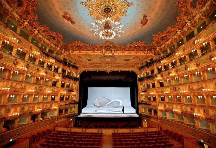 An empty Gran Teatro La Fenice, characterised by golden details and red velvet seats, alongside a painted ceiling.