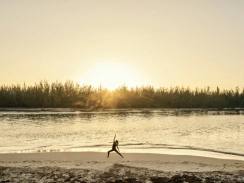 Woman practicing yoga on a beach at sunset