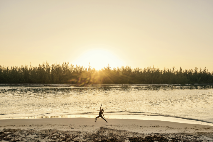 Woman practicing yoga on a beach at sunset