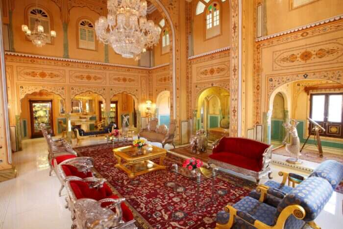 The pavilion suite lounger at the Raj Palace with rich red furniture and a huge chandelier