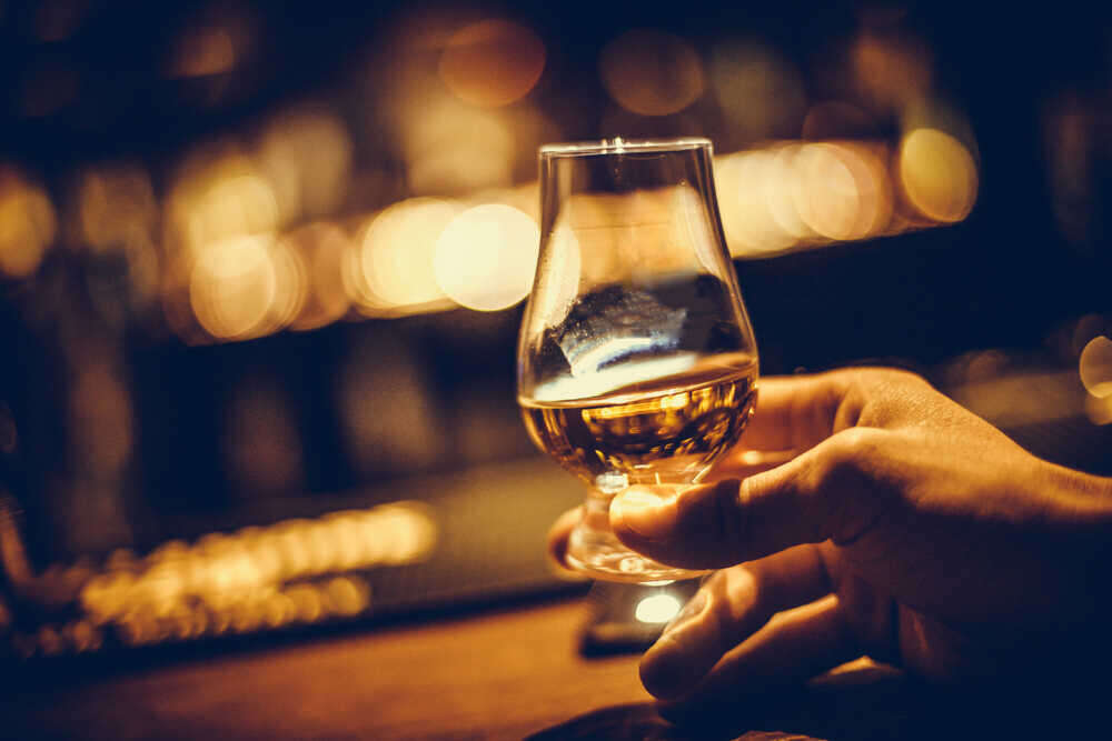 Hand holding a whiskey tasting glass- Difference between Irish Whiskey and Scotch