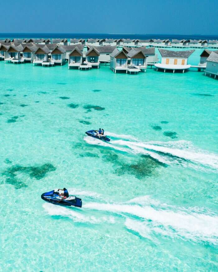 Jet ski's go past over water villas at Mövenpick Resort Kuredhivaru Maldives