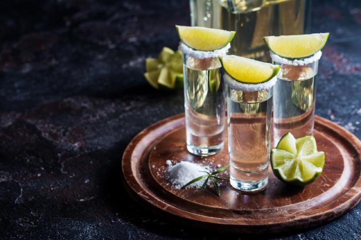 Tequila shots with salted rims, accompanied by lime wedges on a wooden tray