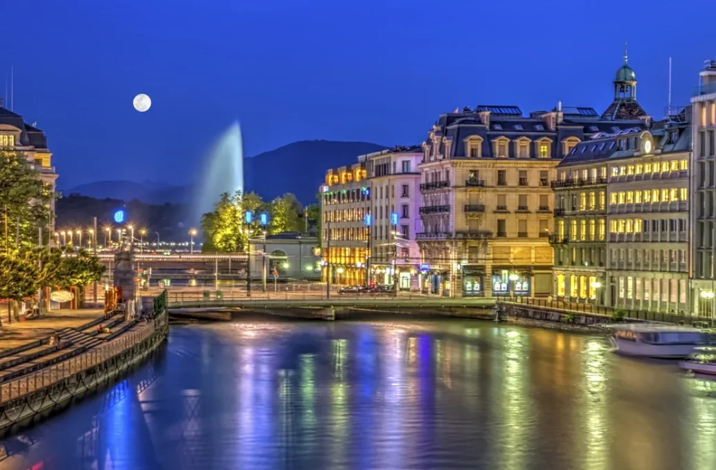 Geneva at night, the moon shining on the water and the buildings golden for the lights