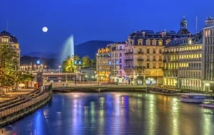 Geneva at night, the moon shining on the water and the buildings golden for the lights