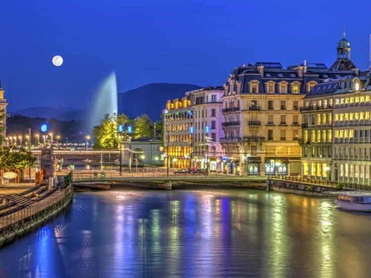 Geneva at night, the moon shining on the water and the buildings golden for the lights