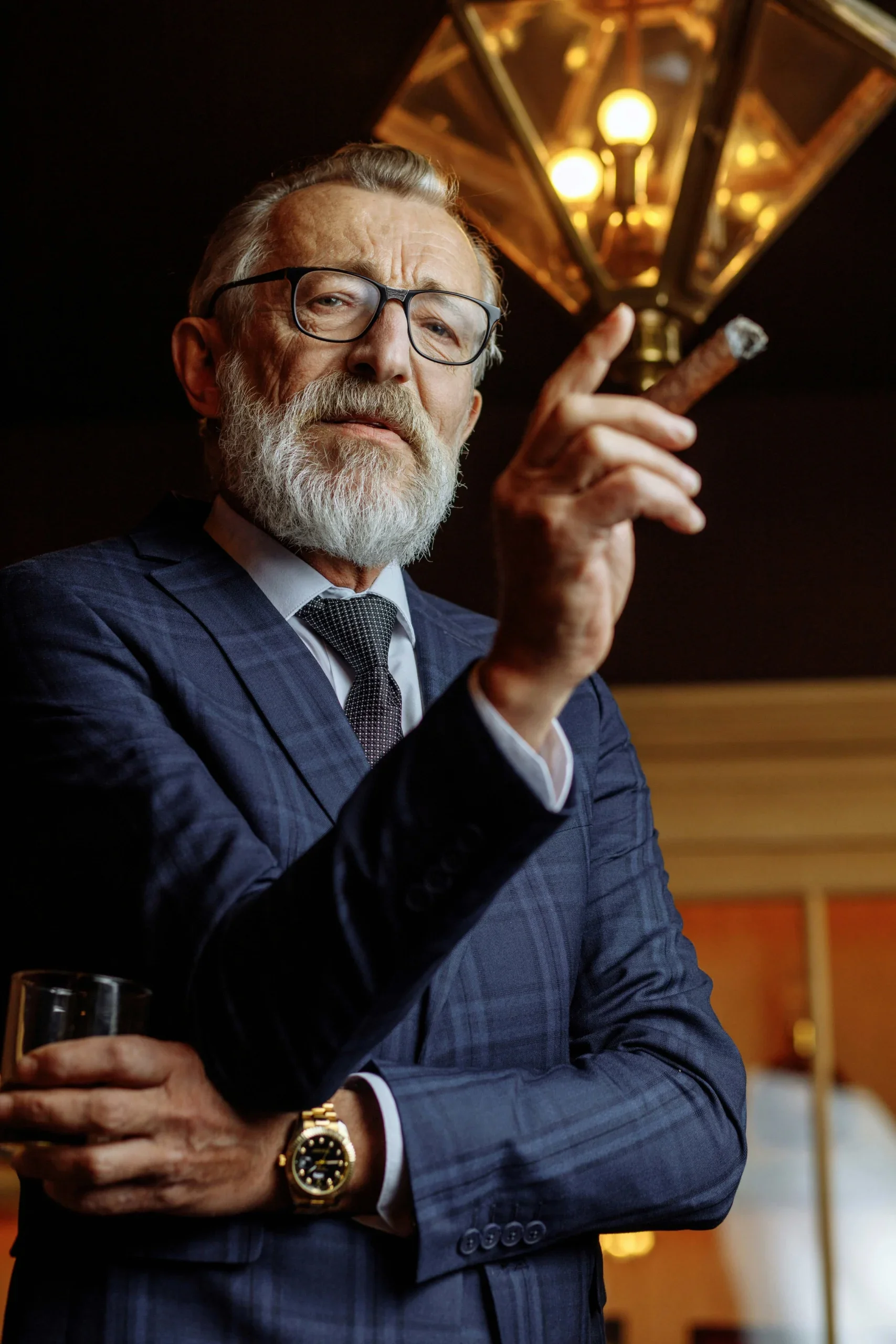 Man smoking cigar with glass of Cognac while wearing Rolex watch